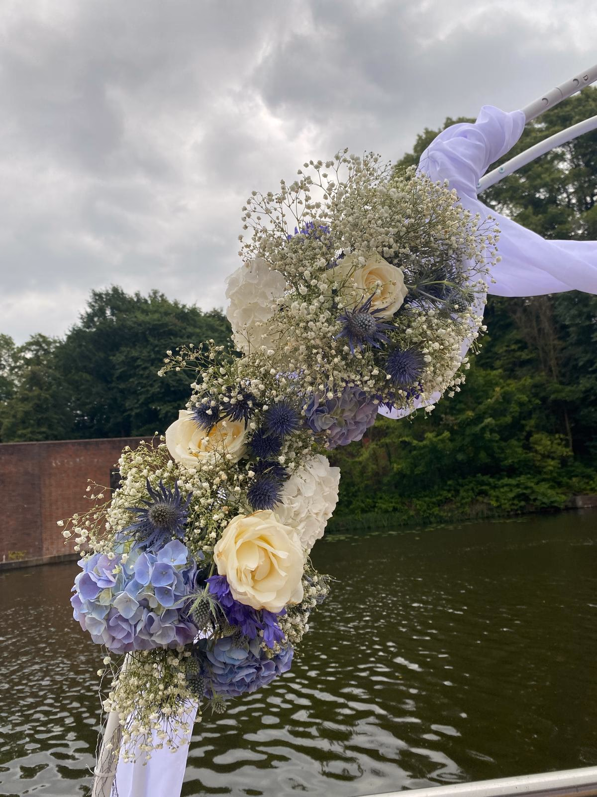 Traubogen-Bogen mit Hortensie, Rose, Schleierkraut und Distel über dem Wasser mit weißem Chiffon.