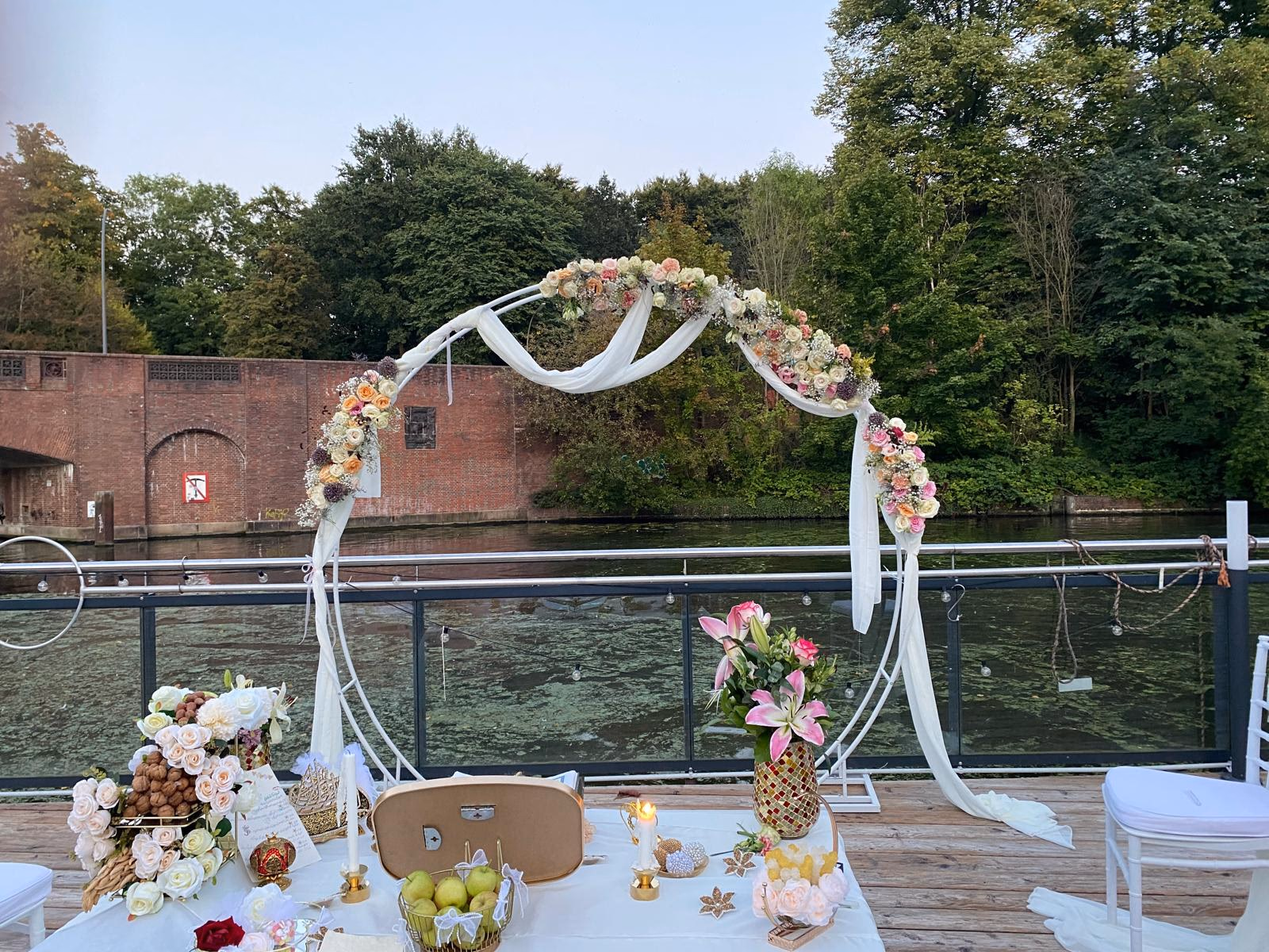Floraler Rundbogen mit Rosen, Hortensien und Schleierkraut am Wasser in Abendstimmung.